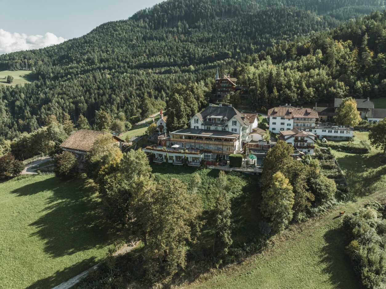 Luftaufnahme der gesamten Anlage des Gasthof Kohlern inmitten von Grün an einem bewaldeten Berghang