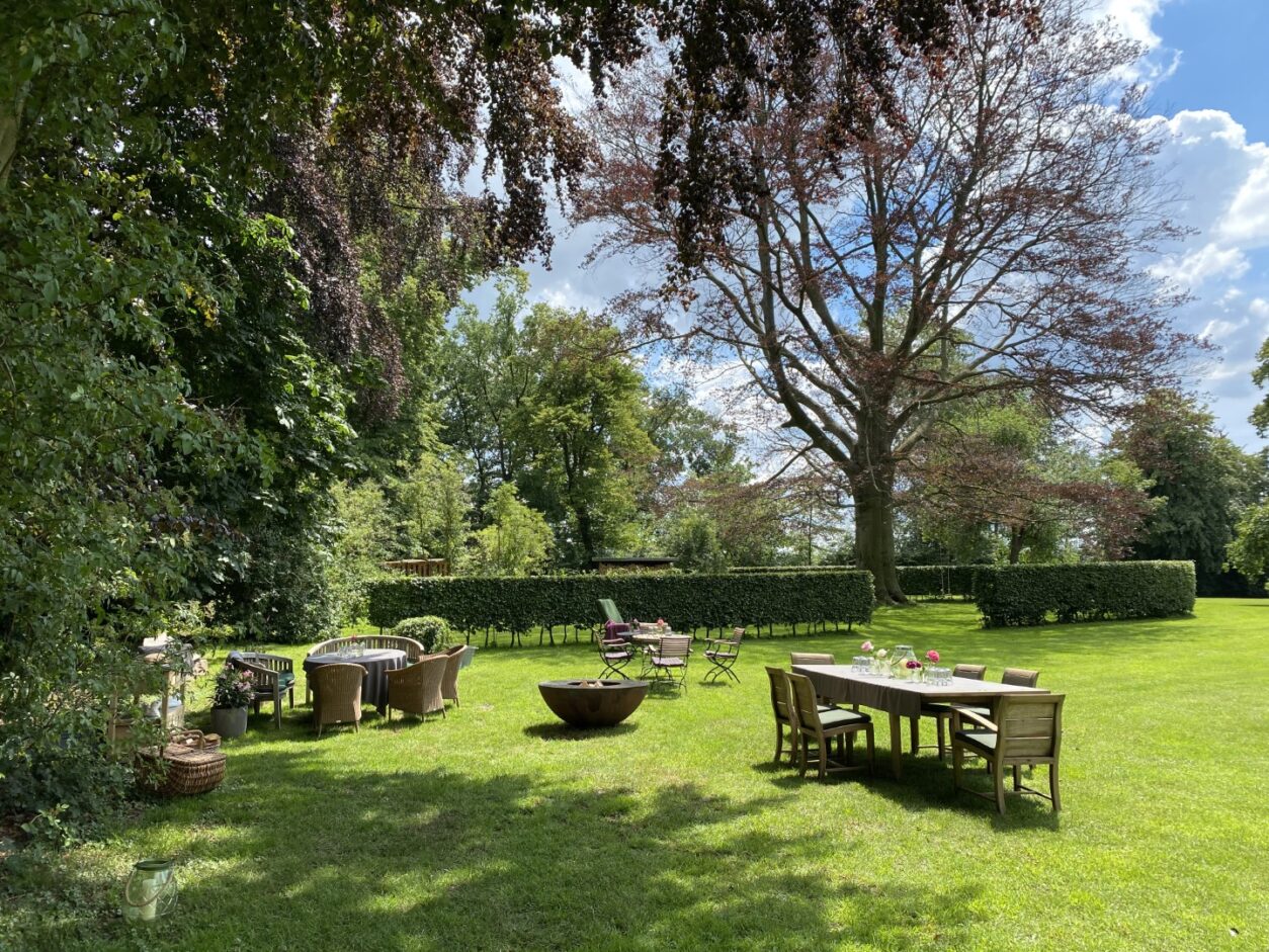Verschiedene Gartenmöbel laden Gäste zum Speisen oder Verweilen im gepflegten, grünen Park ein