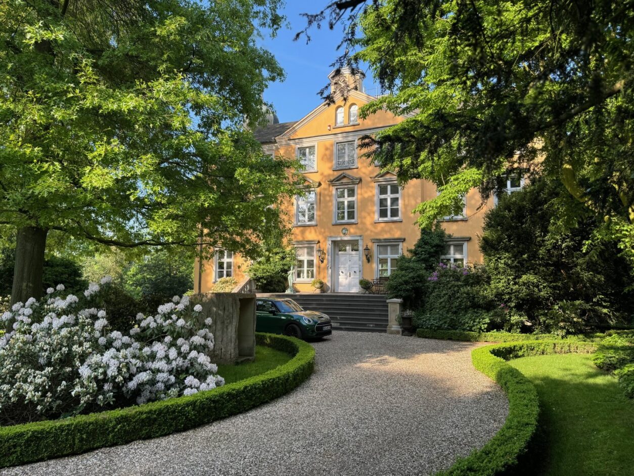 Die hell gekieste Zufahrt, grüne Bäume und die strahlend orange Fassade bilden einen beeindruckenden Kontrast