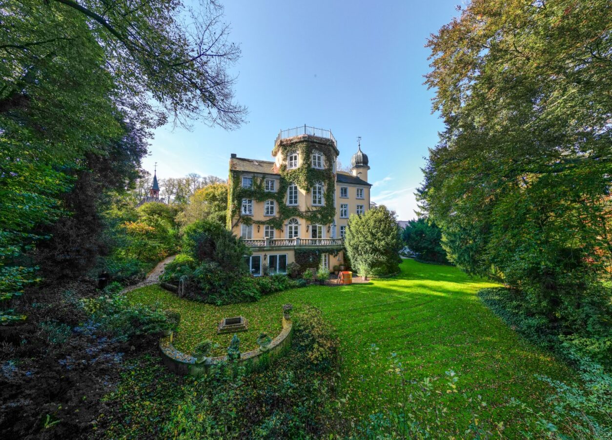 Blick auf die Efeu-bewachsene, rückseitige Fassade von Haus Fürstenberg und die umgebende grüne Gartenanlage