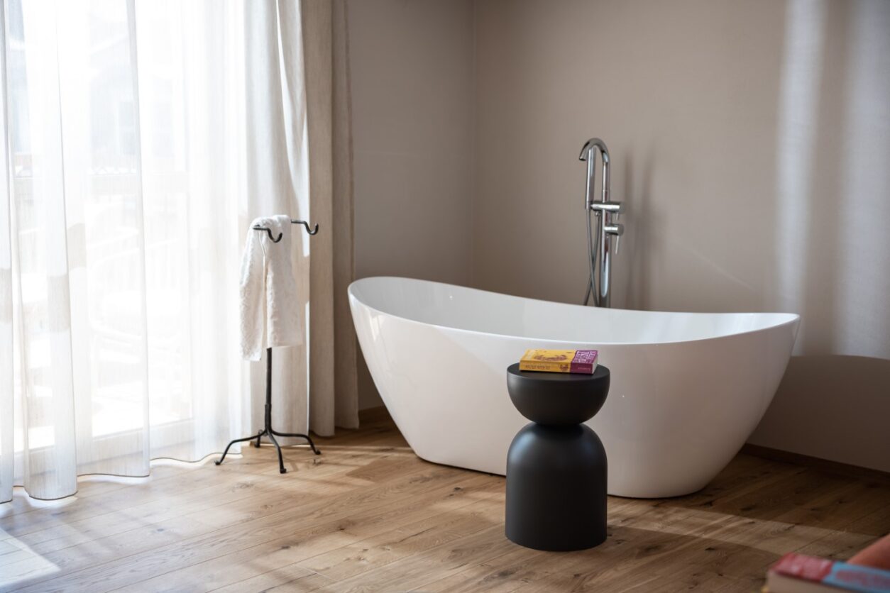 In einer der Ferienwohnungen Kaltern mit Holzdielenboden steht eine moderne Badewanne frei im Raum am Fenster