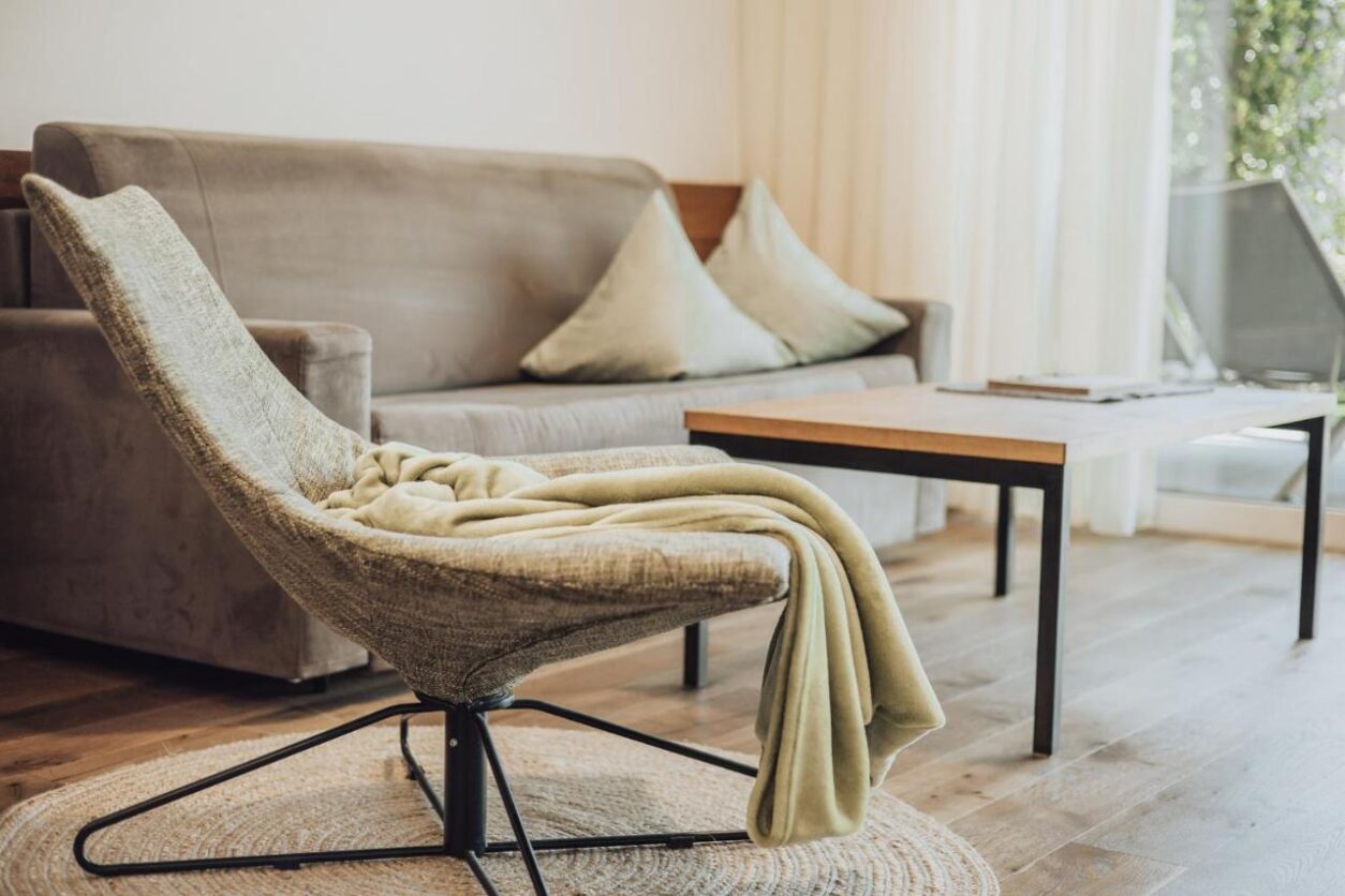 Detailaufnahme der Sitzecke mit Stoffsofa samt Kissen, Tischchen und einer Art Korbstuhl