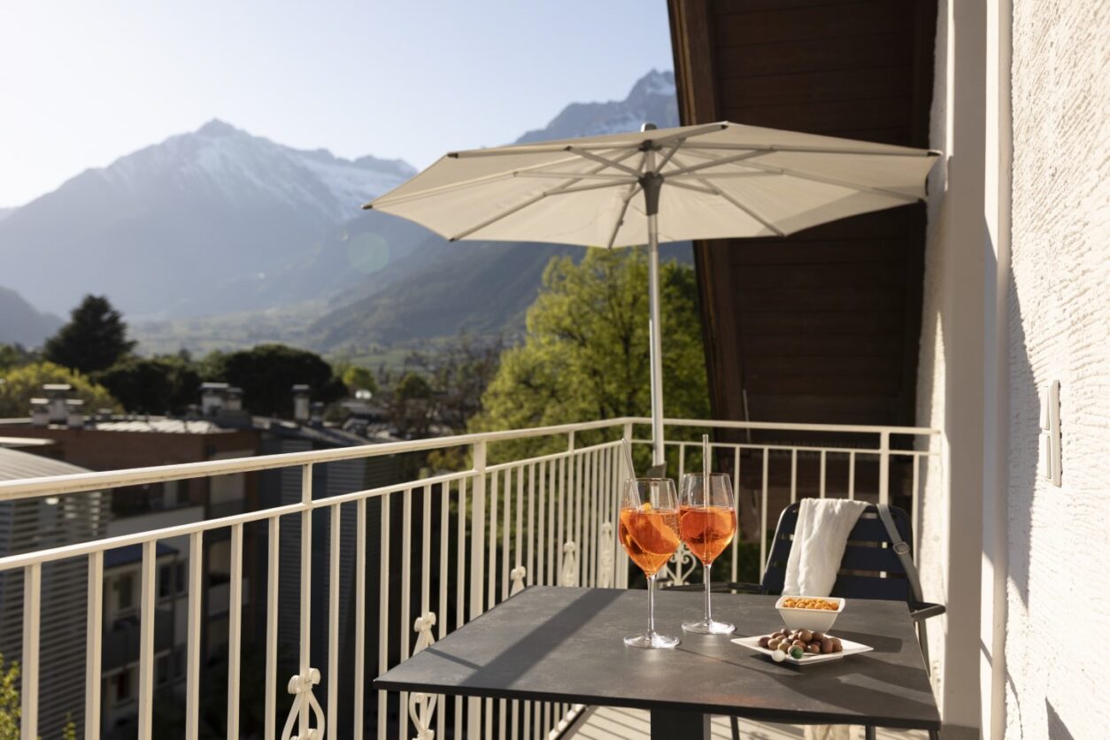 Auf dem Balkon einer Ferienwohnung Meran im Ladurnerhof steht ein Sonnenschirm sowie zwei Cocktails auf dem Tisch bereit