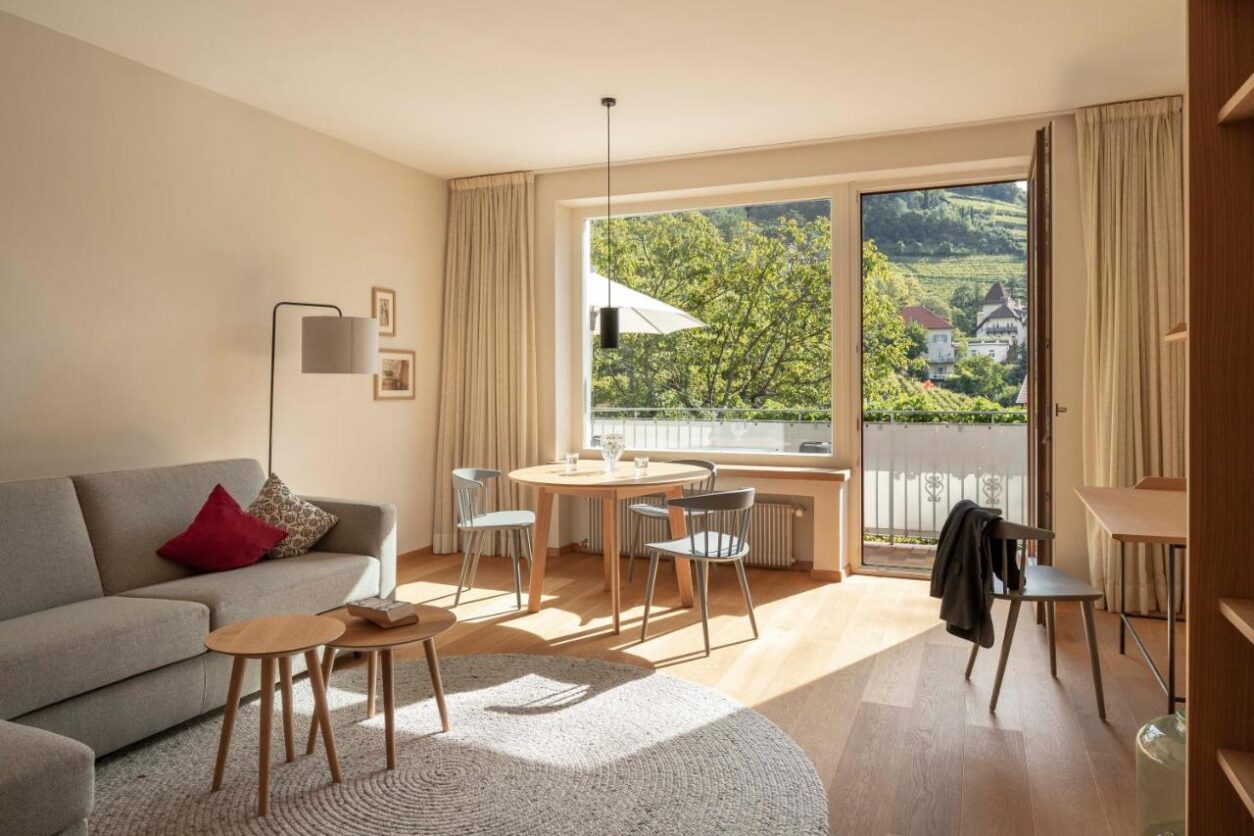 Wohn- und Essbereich einer Ferienwohnung Meran mit stilvollen Holzmöbeln und großen Fenstern