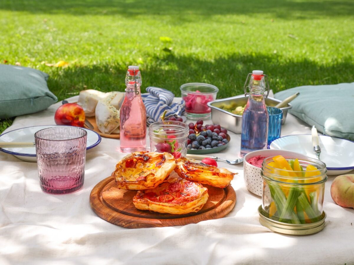 Vegetarisches Picknick auf einer Wiese mit Ei-Kresse-Sandwiches, Tomaten-Tarte-Tatins, Rote-Bete-Hummus und Green-Goddess-Kartoffelsalat