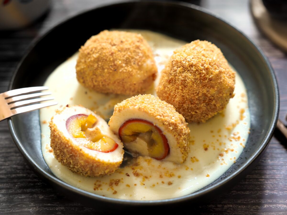 Topfen-Zwetschgen-Knödel in Haselnussbröseln mit Vanillesoße auf einem Teller
